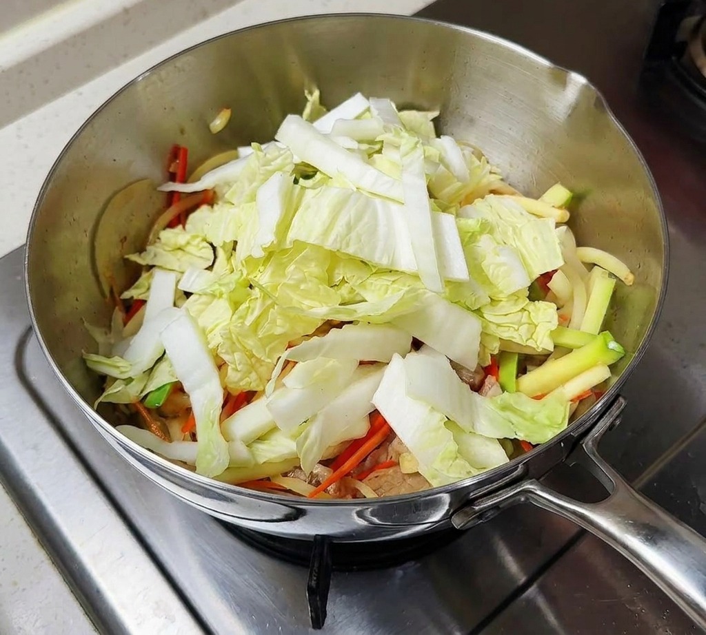 A pile of chopped light green cabbage and sliced dark shiitake mushrooms inside the cooking pot.