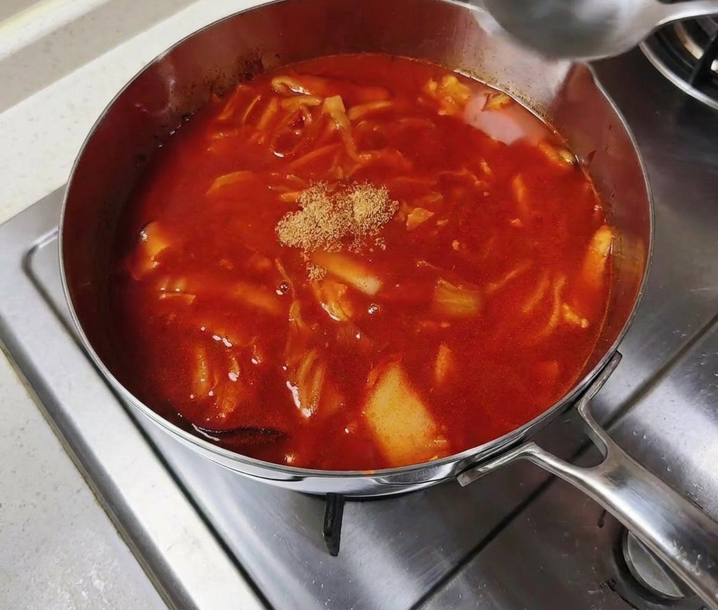 A small mound of tan-colored beef bouillon powder sitting in the center of a pot of simmering red spicy broth.