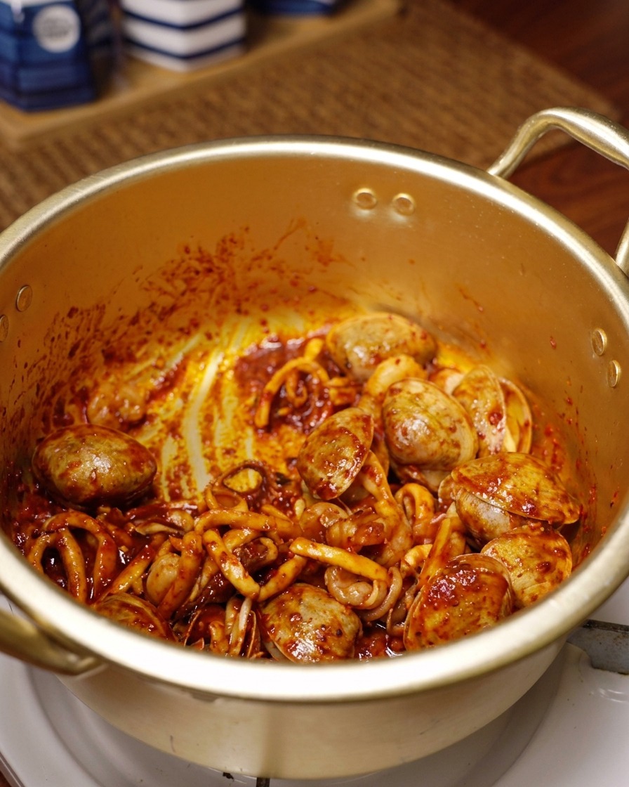 Squid, shrimp, and clams coated in vibrant red chili and spices being stir-fried in a golden pot.