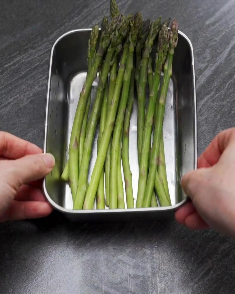 A stainless steel tray filled with bright green asparagus spears that have been chopped into bite-sized pieces.