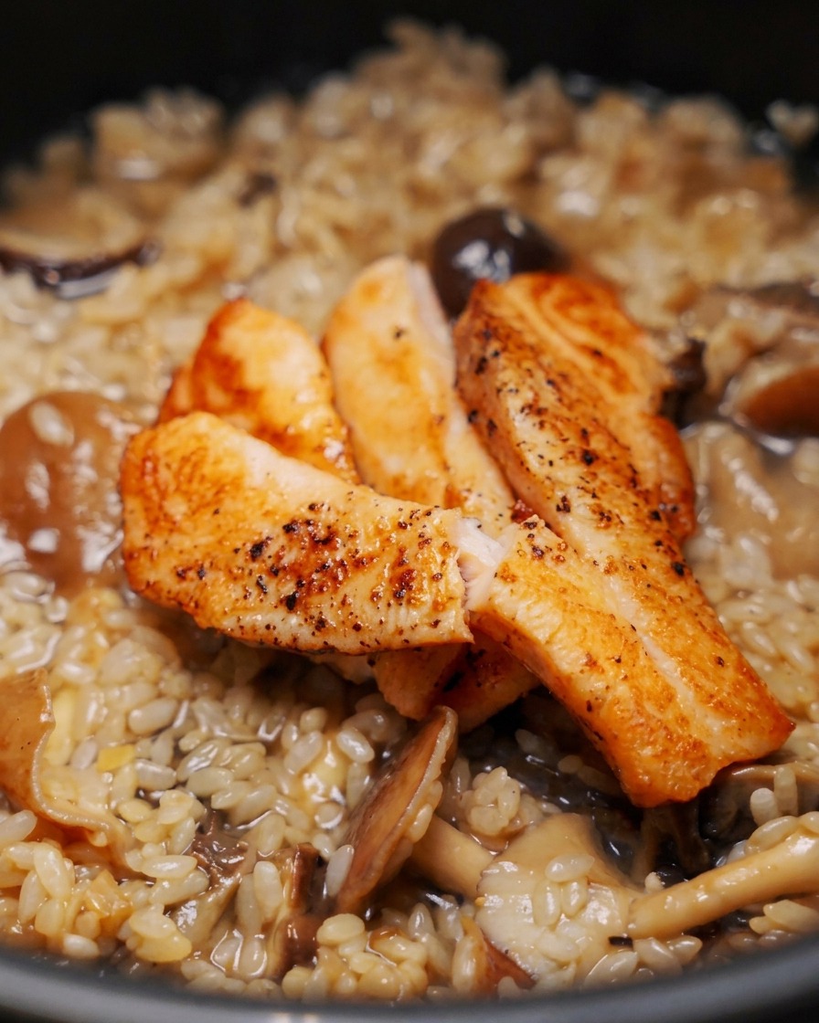 Three pieces of seared, golden-brown salmon fillets resting on top of uncooked rice and mushrooms in a rice cooker.