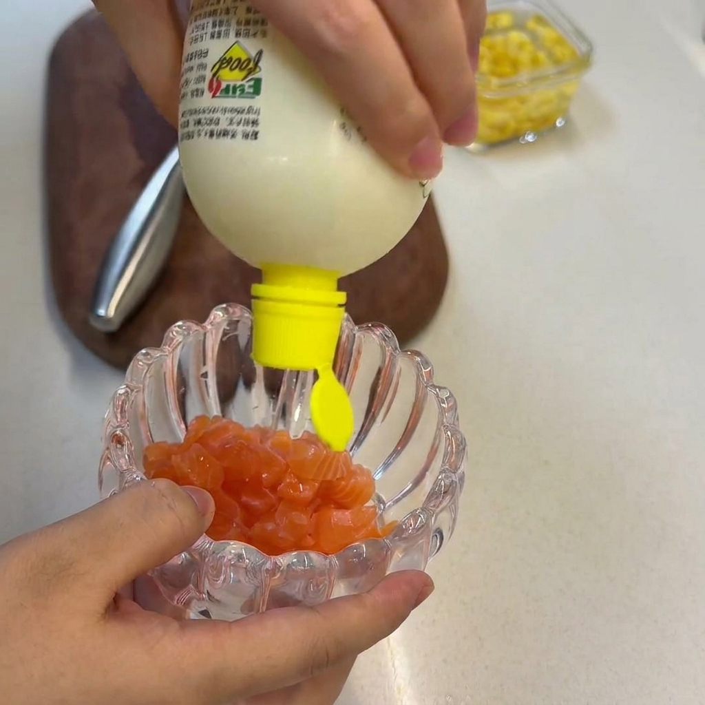 Fresh lemon juice being squeezed from a yellow squeeze bottle onto a pile of raw salmon cubes inside a decorative glass bowl.