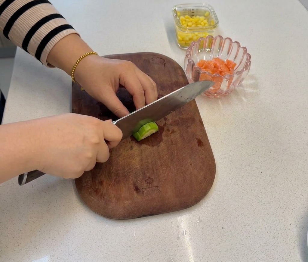 A hand slicing through a broccoli stem with a knife on a wooden board to create smaller, bite-sized florets.