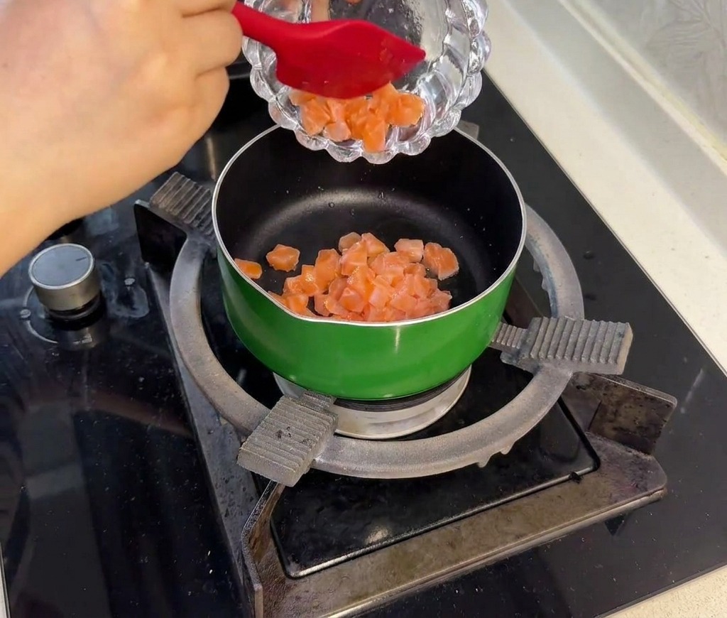 Marinated raw salmon cubes being added to a small green pan and stir-fried until the exterior turns opaque and light pink.