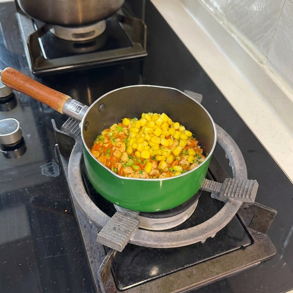 A heap of bright yellow blanched corn kernels sitting on top of the salmon carrot and broccoli mixture in the green pan.