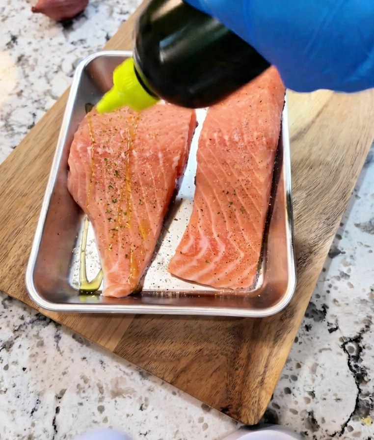 Soy sauce and oil being drizzled over seasoned raw salmon fillets for marination.