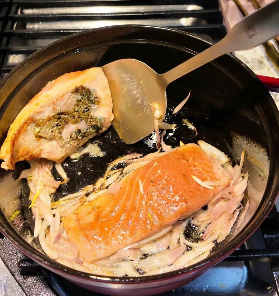 A metal spatula flipping a salmon fillet in a pot, showing a browned and seared surface.