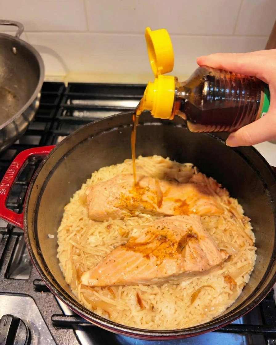 Toasted sesame oil being poured from a bottle with a bright yellow cap over the finished salmon and rice.