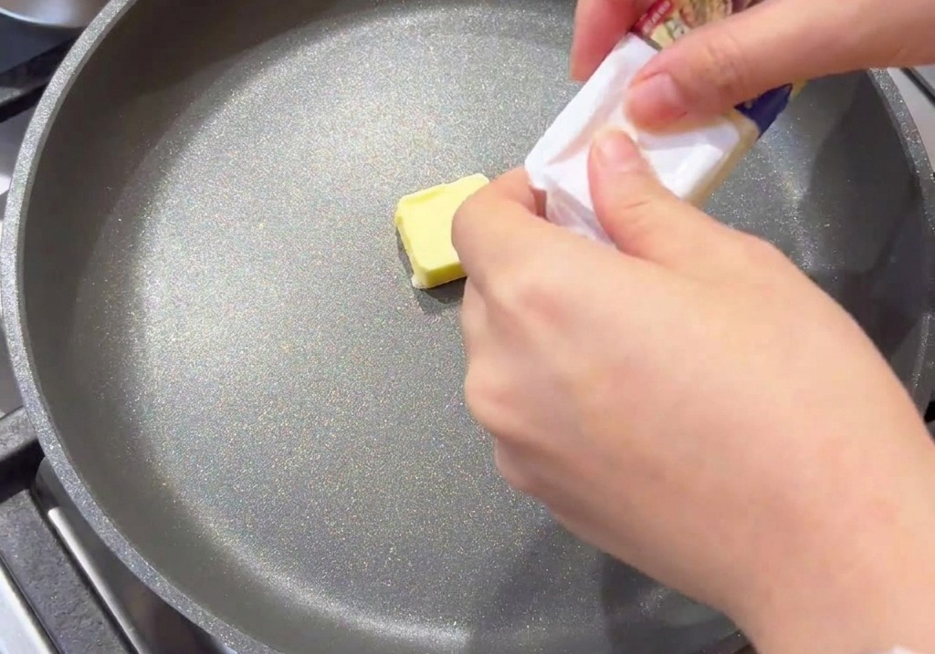 A small square of yellow butter melting in the center of a grey non-stick frying pan.