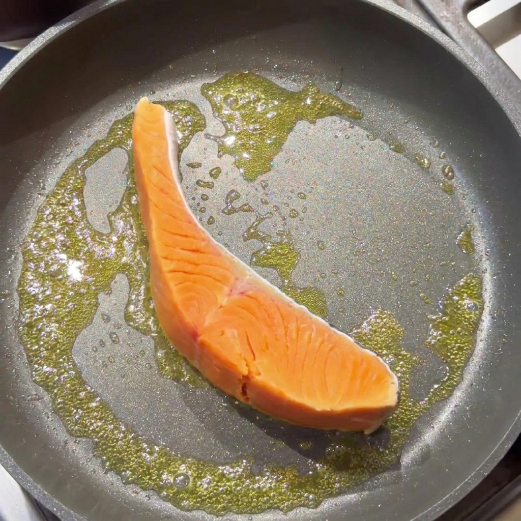 A raw salmon fillet searing in a pan with bubbling melted butter.