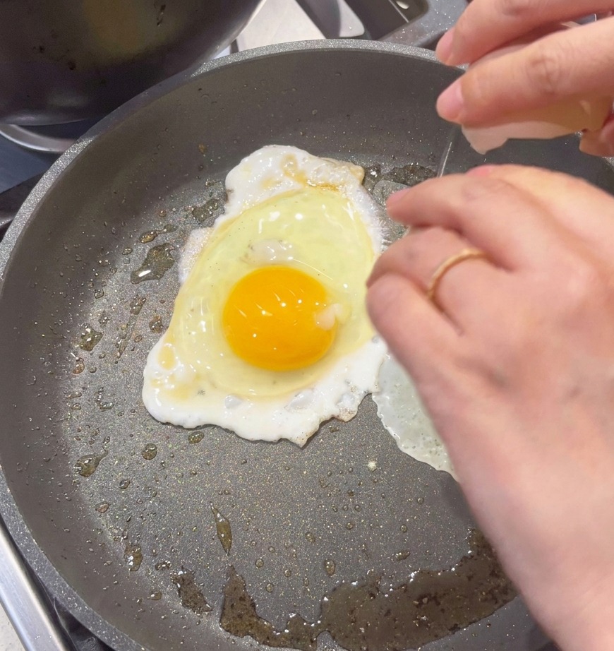 An egg being cracked into a non-stick pan to be scrambled.