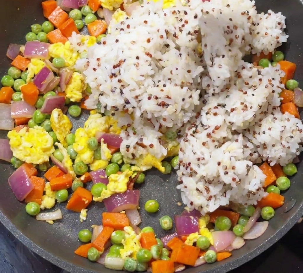 Cooked white rice and quinoa being added to a pan containing sautéed vegetables and eggs.