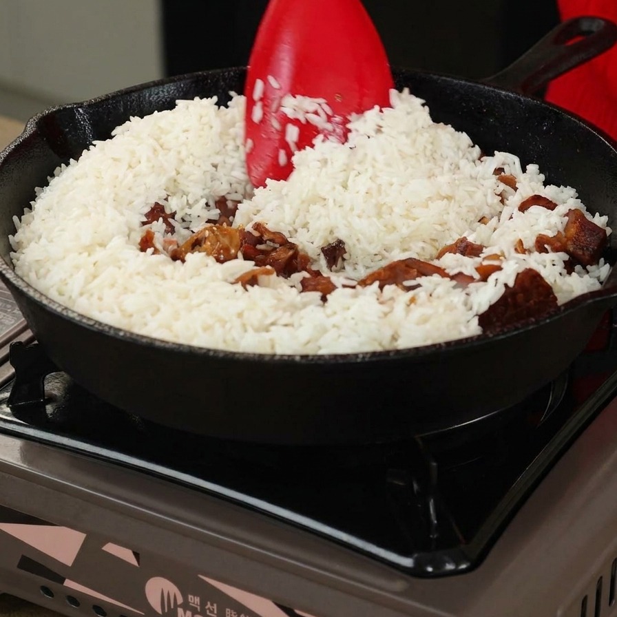Rice and mushrooms being stirred with a red spatula in a cast iron pan.