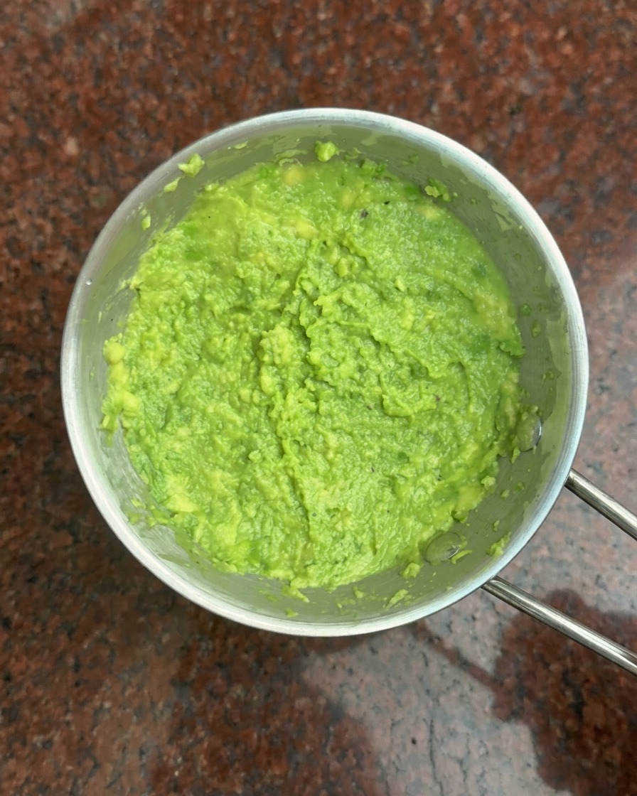 A top-down view of a small metal bowl filled with vibrant green mashed avocado paste.