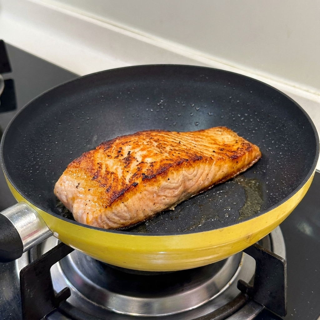 A seared salmon fillet in a yellow pan showing a perfectly browned and crispy surface.
