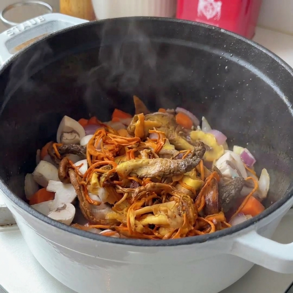 A variety of fresh and dried mushrooms being added to a steaming pot of sautéed vegetables.