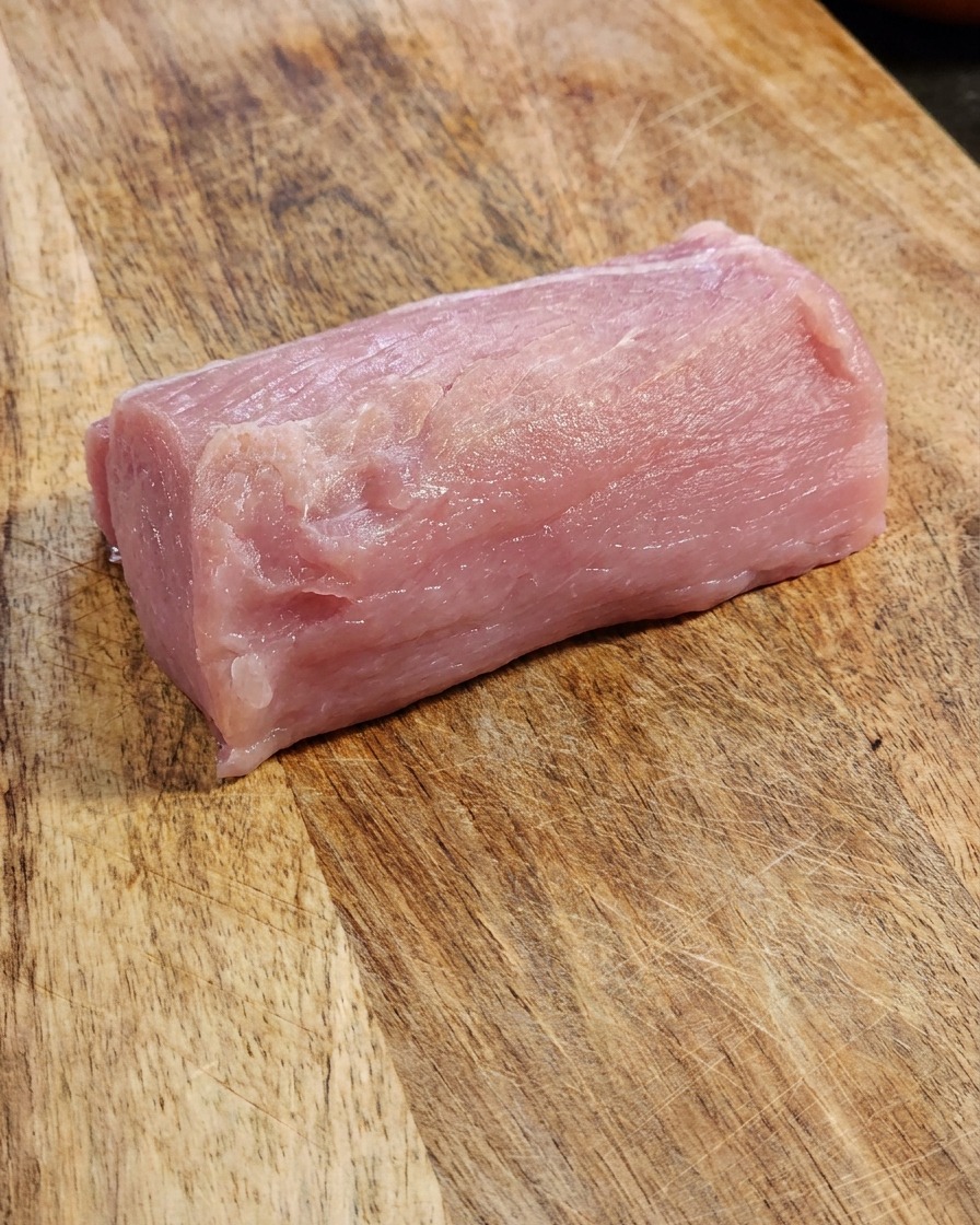 A fresh, thick piece of raw pink pork loin resting on a textured wooden cutting board.