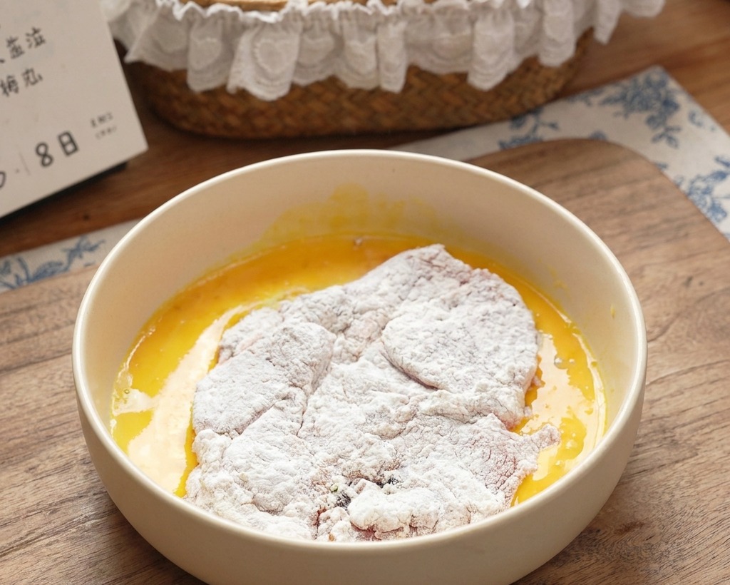 A flour-coated pork chop being submerged into a bowl of bright yellow beaten eggs.