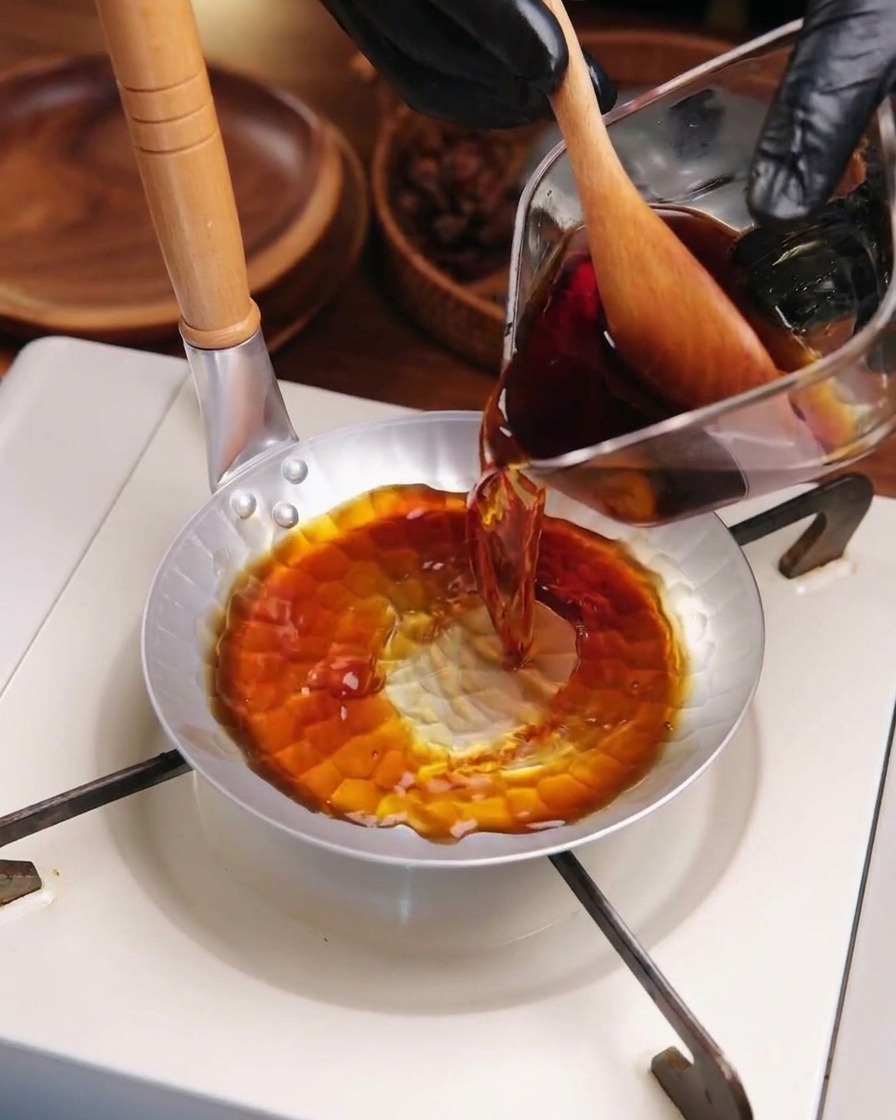 Dark savory katsudon sauce being poured from a glass measuring cup into a small round metal pan on a portable stove.