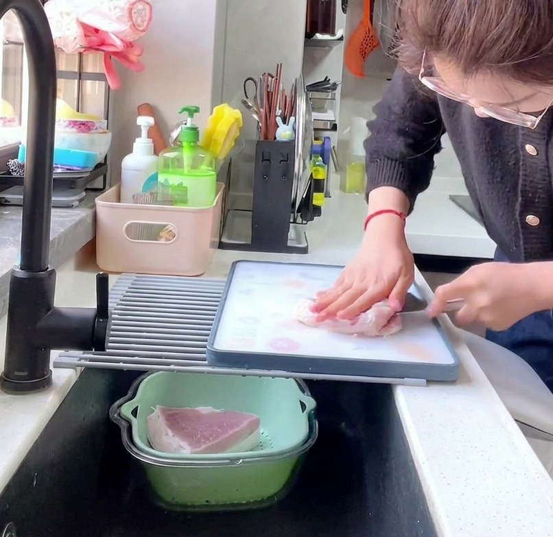 A side view shot of a person using a large kitchen cleaver to cut a raw pork loin into 1cm thick slices on a patterned cutting board