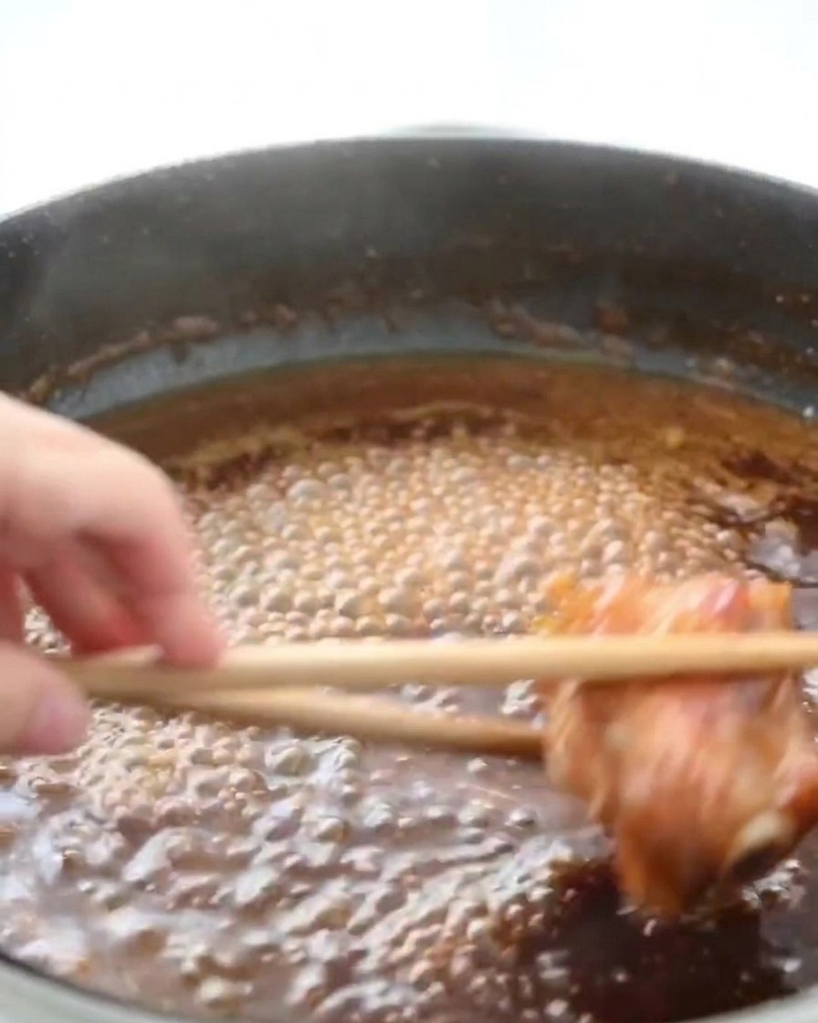 Chicken thighs simmering in a pan of bubbling, dark brown honey sauce with steam rising from the surface.