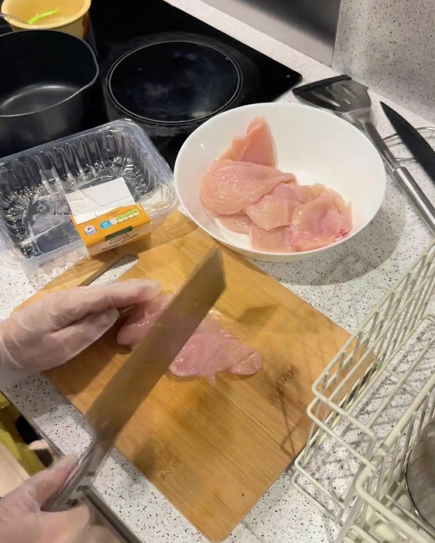 The back of a heavy knife being used to strike a thin chicken fillet on a wooden board to flatten and tenderize it.