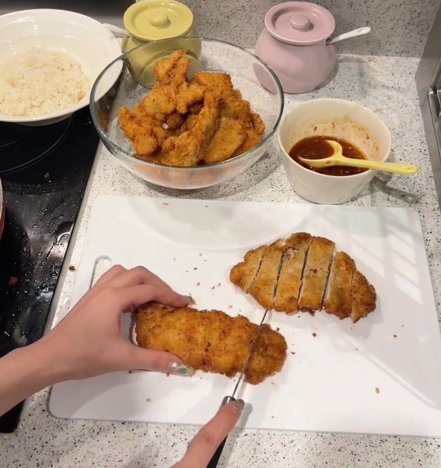 A person slicing a crispy, golden-brown fried chicken cutlet into strips on a white plastic cutting board.