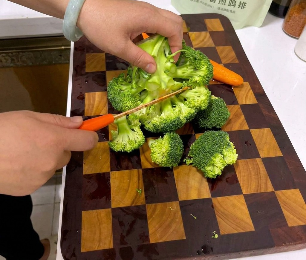 A pair of hands cutting a large head of broccoli into small florets on a wooden checkered cutting board.