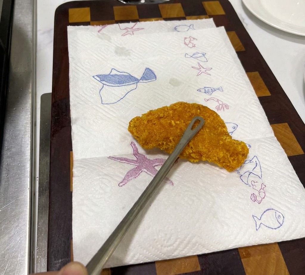 A crispy, golden-brown fried chicken steak resting on a white paper towel with blue sea-life patterns to drain.