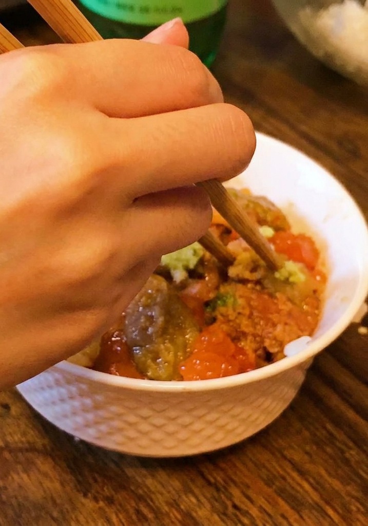 A hand using chopsticks to place a small amount of wasabi onto the center of a sea urchin and salmon roe rice bowl.