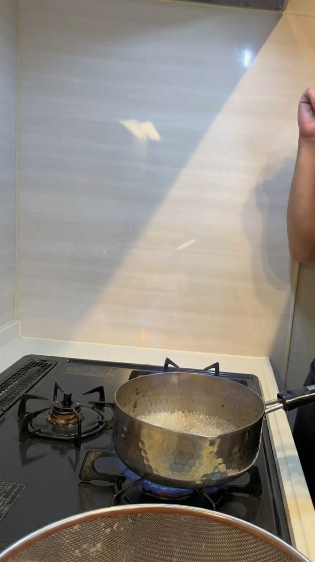 A dramatic blue and orange flame erupting from a small metal pot on a lit gas stove during the flambé process.