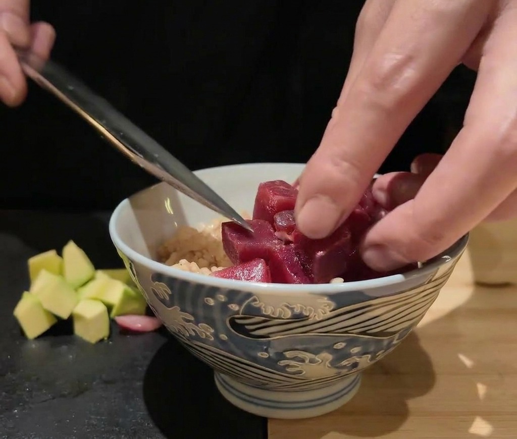Cubed raw seafood and scallops being carefully placed onto a bowl of rice using the side of a knife.