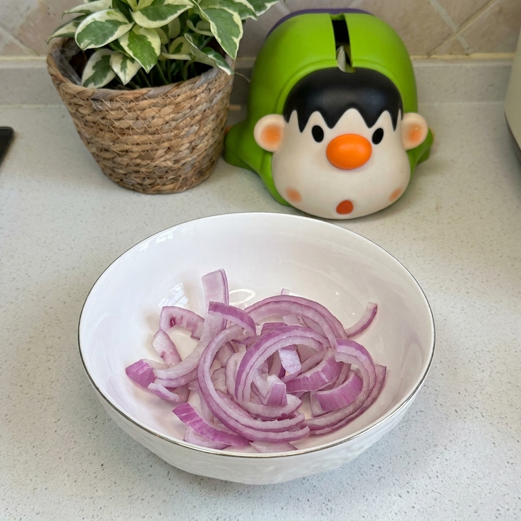 A white ceramic bowl sitting on a countertop containing several fresh, purple-hued red onion rings.