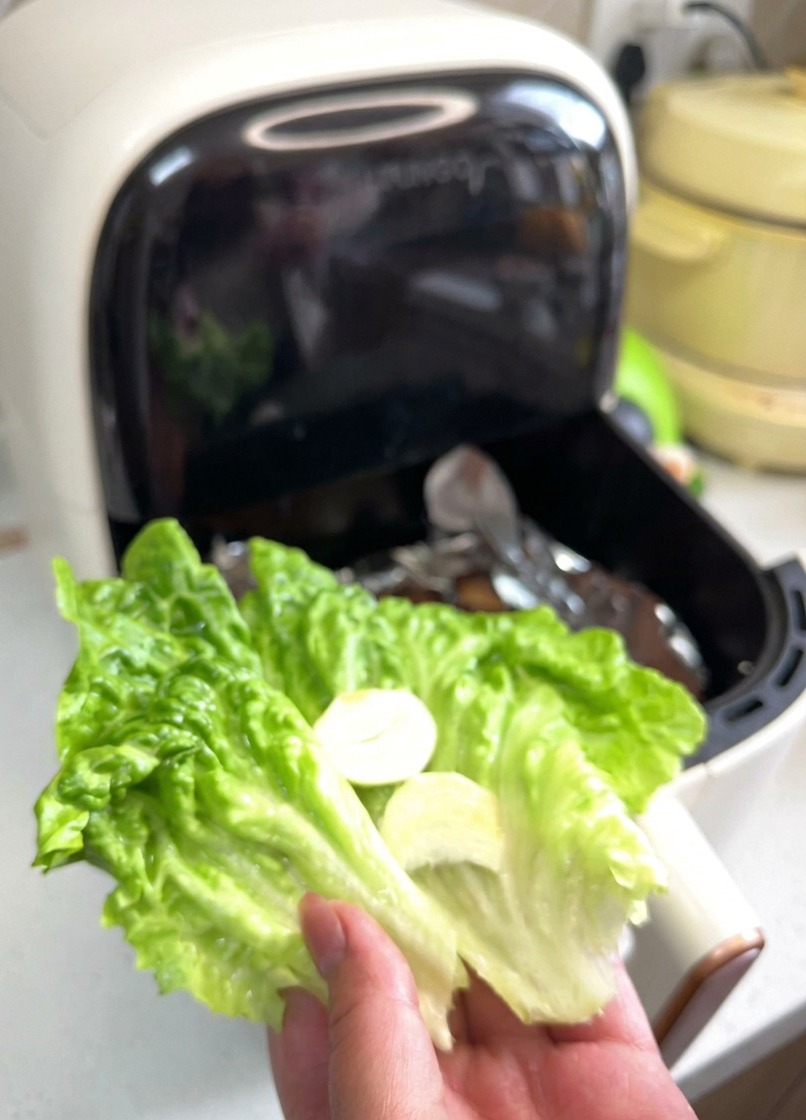 A hand holding a vibrant green lettuce leaf topped with two thin slices of white garlic and red onion rings.