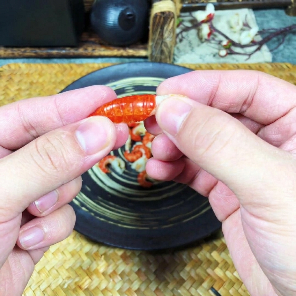 Close-up of hands peeling the hard orange shell off a cooked crawfish tail to reveal the white meat inside.