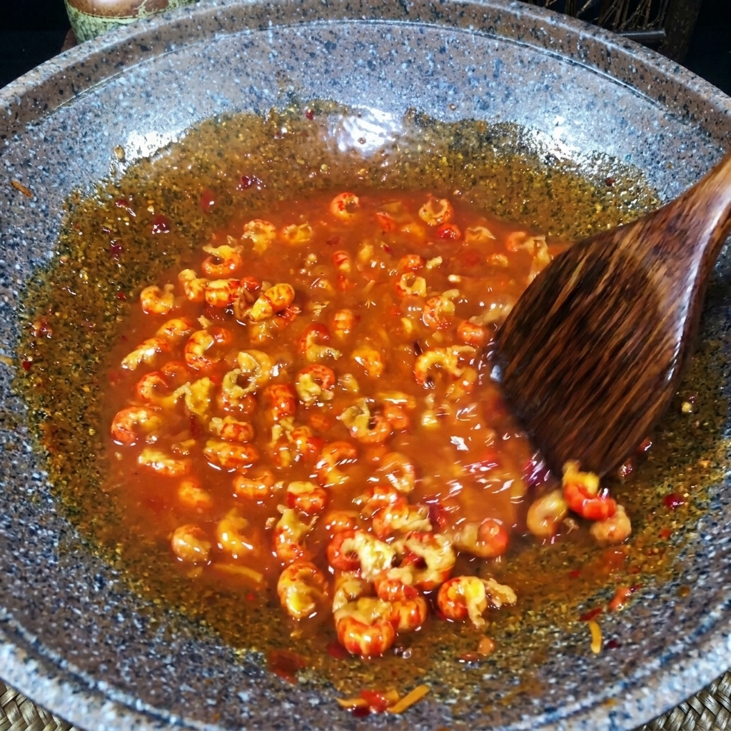 A wooden spatula stirring crawfish tails in a thick, bubbling red gravy in a stone pan.