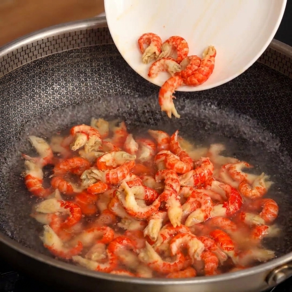 A white plate tilting to slide peeled crayfish tails into a pan of bubbling, boiling water.