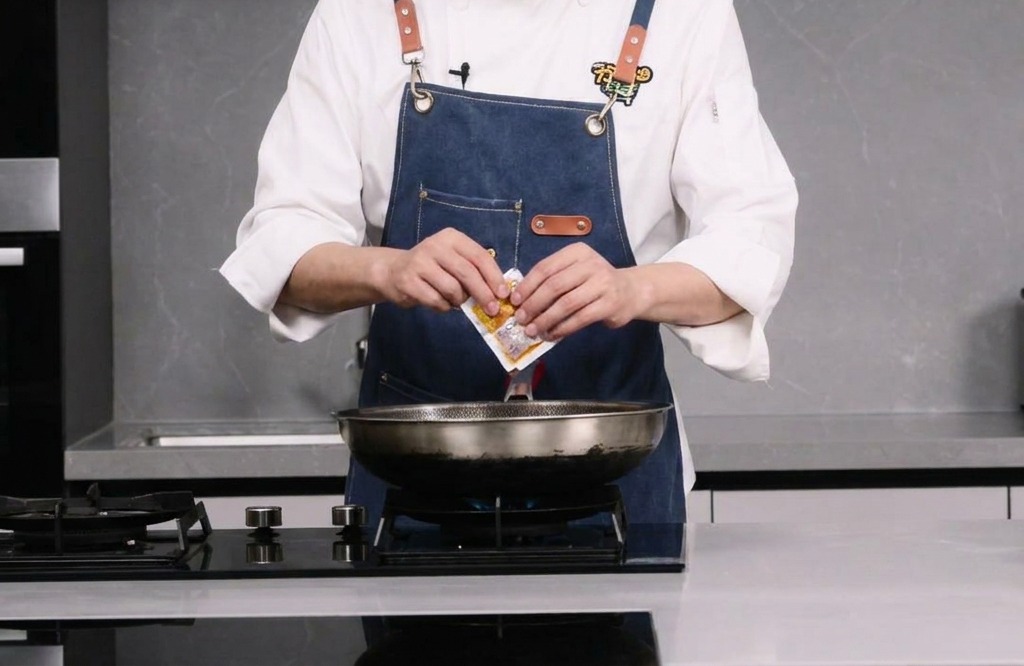 A person tearing open a small packet of spicy hot pot base over a wok.
