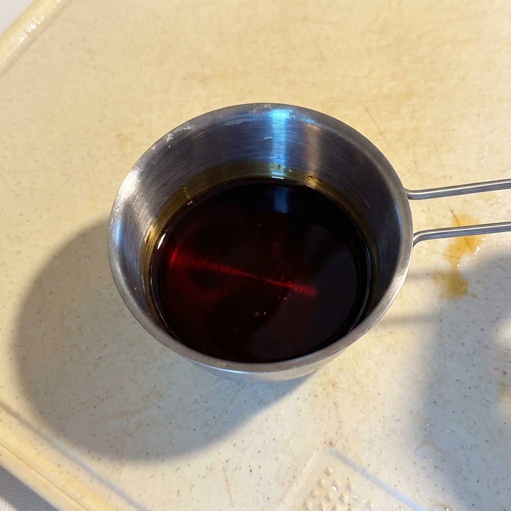 A dark, glossy sauce mixture contained in a small stainless steel measuring cup.