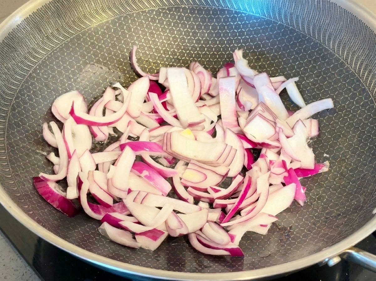 Slices of vibrant red onion being stir-fried in a textured metal pan.
