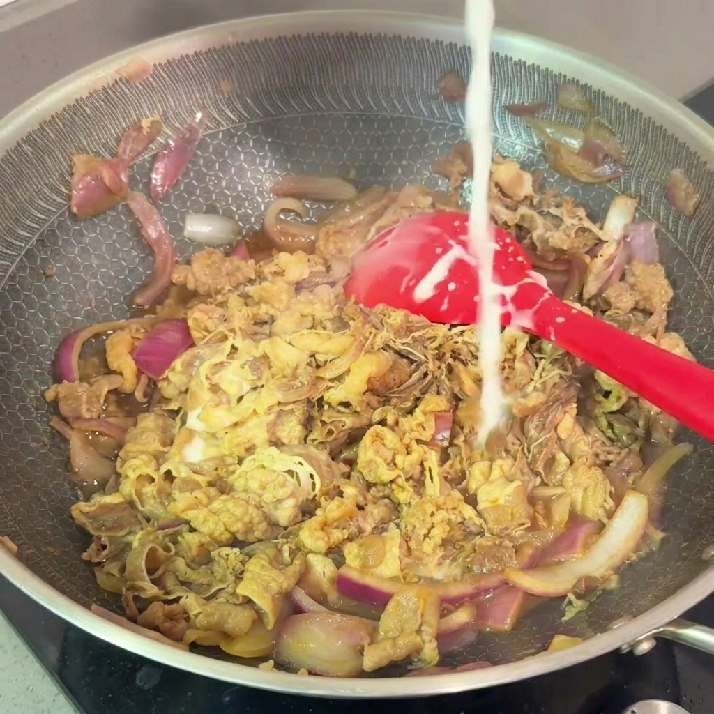 A thin stream of white starch slurry being poured into a pan of simmering beef and onions.