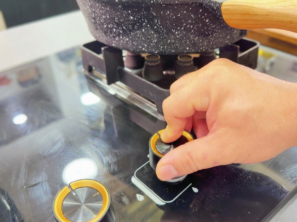 A hand turns the knob of a gas stove to ignite the flame under a dark, stone-textured wok.