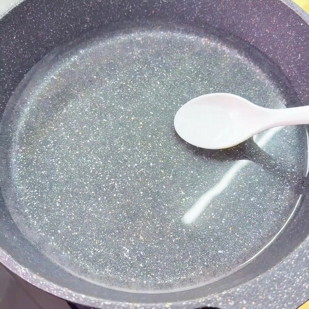 A white spoon adds a portion of salt into a wok filled with clear, cold water.