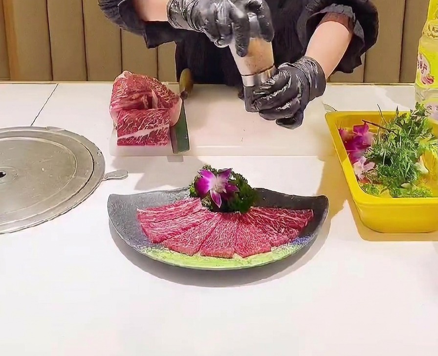 A grinder being used to distribute pink salt crystals over a decorative arrangement of raw marbled beef slices.
