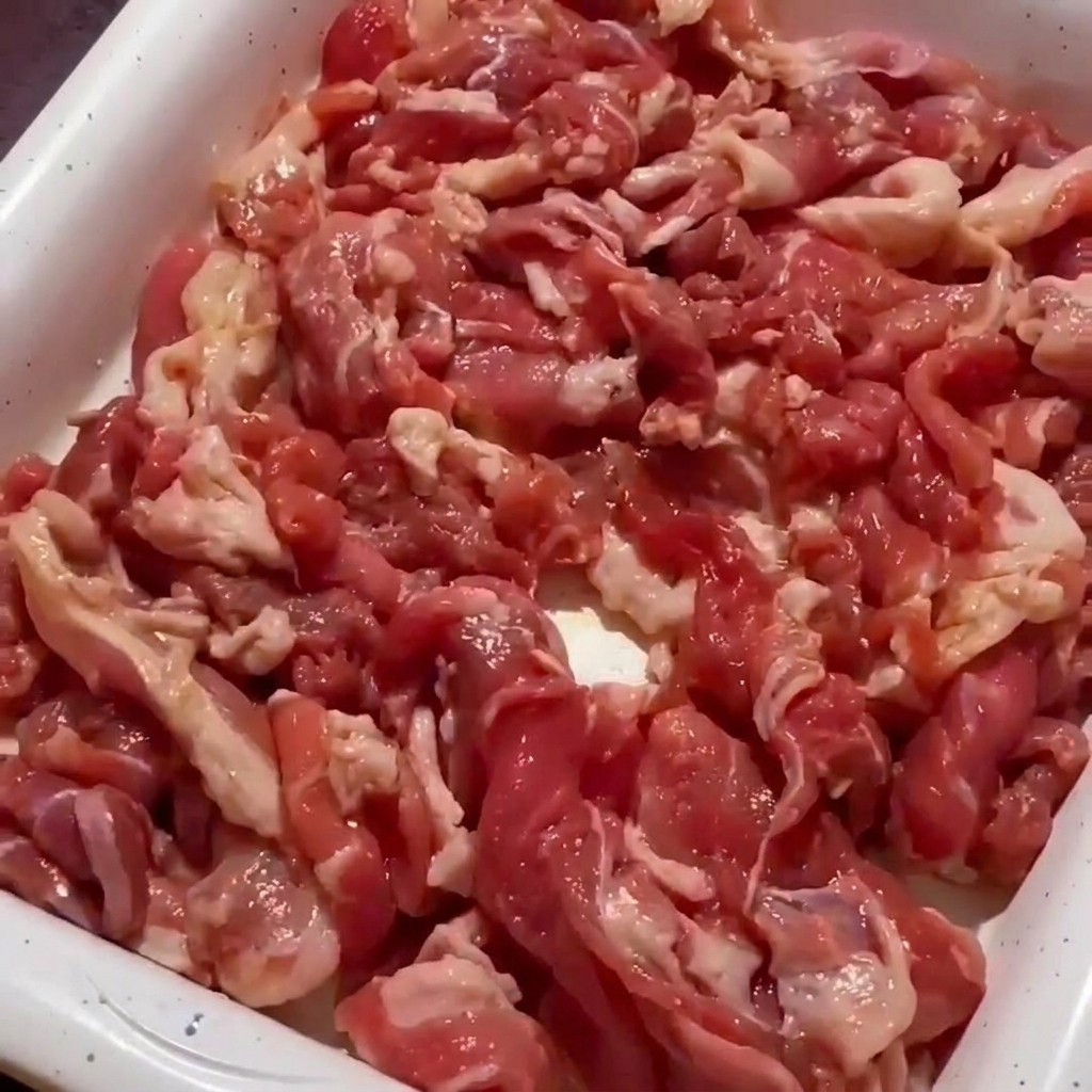 A close-up of pork meat being stir-fried in a pan until the edges are browned and the meat is mostly cooked.