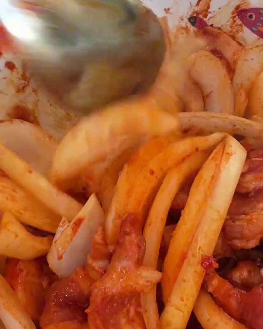 Large slices of raw white onions being folded into a bowl of spicy red marinated pork.