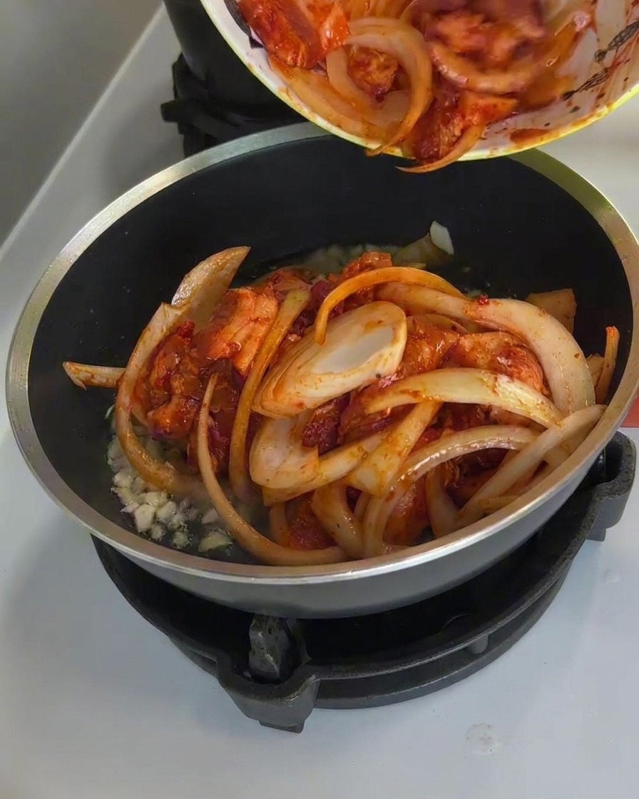 Spicy pork and onions being cooked in a pan, with steam rising and the sauce bubbling.