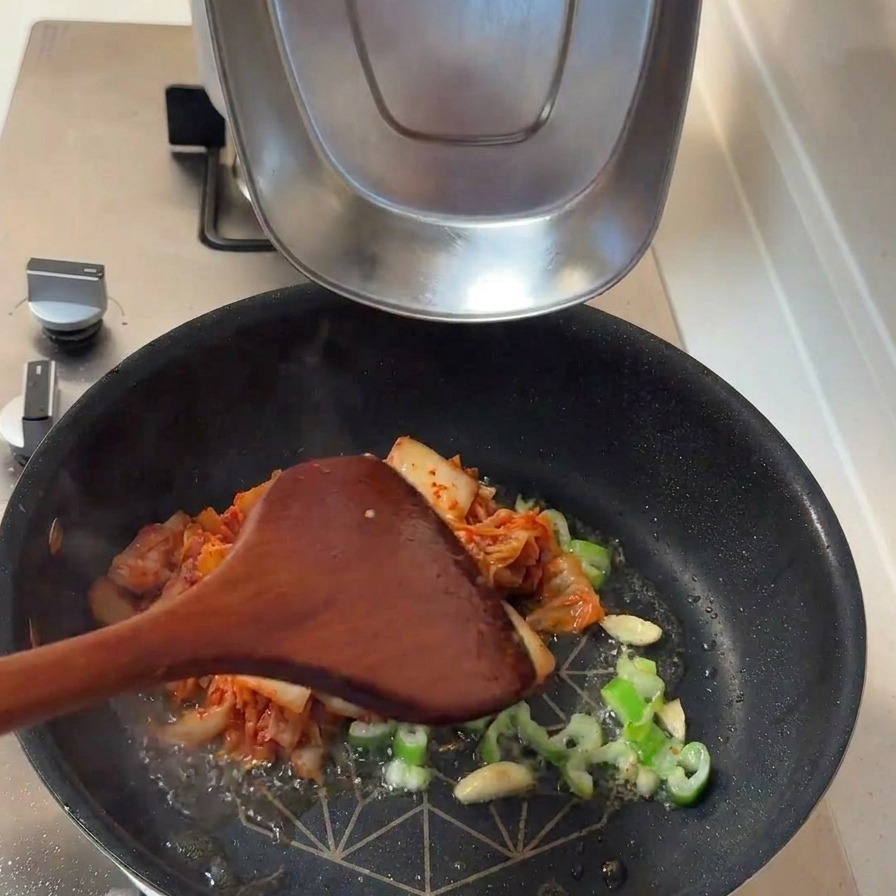 Fermented kimchi and thick white onion slices being added to the pan with sautéed aromatics.