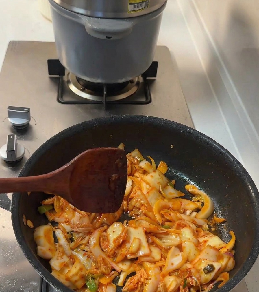 Liquid seasoning and granulated sugar being mixed into the sautéing kimchi and onions.