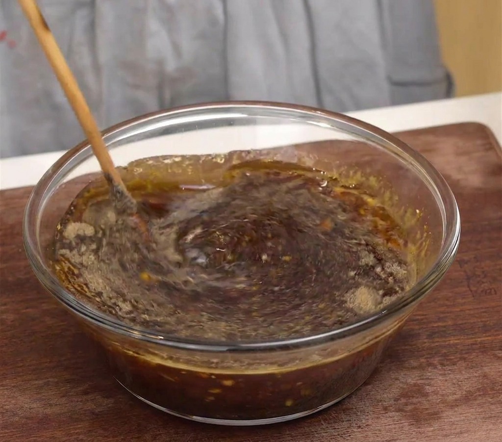 A wooden spoon stirring a dark, aromatic Korean beef marinade in a clear glass mixing bowl.